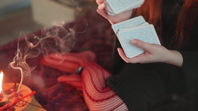 Smoky caucasian tarot ritual with incense, redhaired woman shuffling cards near burning incense and drifting smoke, warm textiles and focused hands create moody boho divination scene