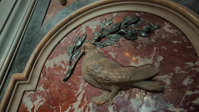 Close-up views of historic marble statues and a beautifully carved dove with an olive branch medallion inside the magnificent Saint Peter's Basilica located within Vatican City, Rome, Italy.

