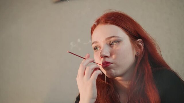 Young redhead smoking long cigarette holder, moody indoor portrait of contemplative fortune teller blowing incense smoke, vintage makeup and eyeliner, tarot hints off frame, warm soft lighting,