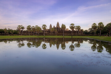 Fototapeta premium Angkor Wat temple complex in Siem Reap, Cambodia, reflected in a pond at sunset. This iconic UNESCO World Heritage site is a breathtaking example of Khmer architecture.