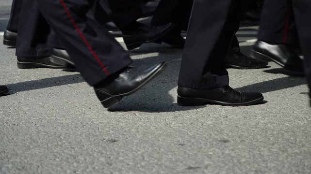 Close-up of uniformed marchers' polished black shoes stepping in unison along an urban street during a formal procession, followed by an empty roadway with double lane markings.