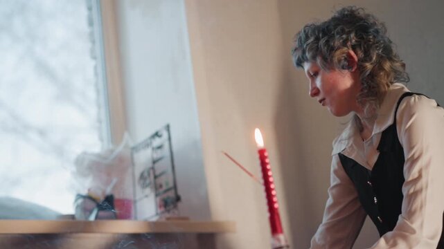 Caucasian teller converses with caucasian seeker by window with candle between them, shared consultation and exchange of stories, intimate rapport, gentle gestures, narrative mood in cozy domestic