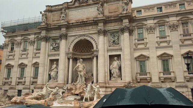 This beautiful panning video reveals the majestic architecture and exquisite baroque marble statues of the iconic Trevi Fountain in Rome, Italy, during a cloudy and rainy autumn afternoon.


