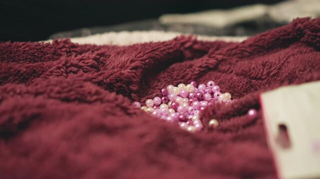 Pink beads on burgundy towel revealing mystic keepsake and tag, soft plush texture, shallow depth of field, warm cinematic lighting, intimate closeup evoking nostalgia and subtle fortuneteller prop