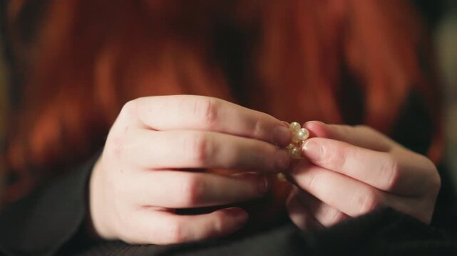 Hands grasp beaded jewelry. Intimate scene showing hands clutching colorful beaded ornaments softly lit. Softly illuminated setting where fingers grasp decorative beads with affectionate intent