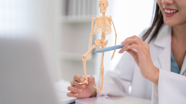Asian female doctor explaining skeletal anatomy bone structure using model teaching patient medical education healthcare professional demonstrating orthopedic