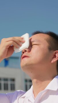 Vertical video, Asian man wipes sweat off his face with tissue paper in sweltering summer heat.