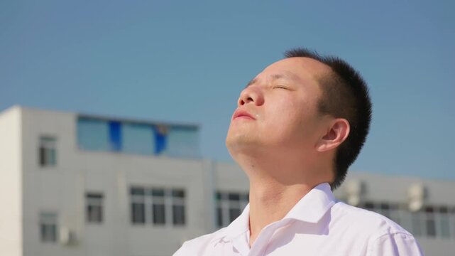 Asian man wipes sweat off his face with tissue paper in sweltering summer heat.