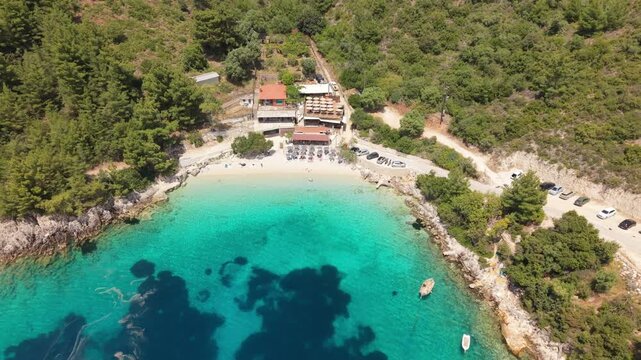 Aerial drone footage slowly pulling back from a beautiful hidden beach surrounded by lush green hills and crystal-clear turquoise water. 