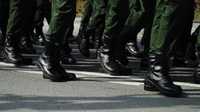 Detailed close-up of synchronized soldiers' black boots and green uniforms marching in tight formation along an asphalt street during a disciplined parade, emphasizing cadence, order, and unity
