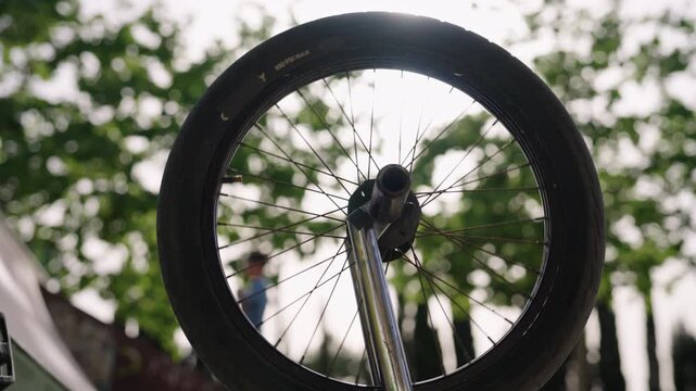 Close up of BMX front wheel with shallow depth of field as a child rides a scooter blurred in background at a skatepark. Urban lifestyle scene