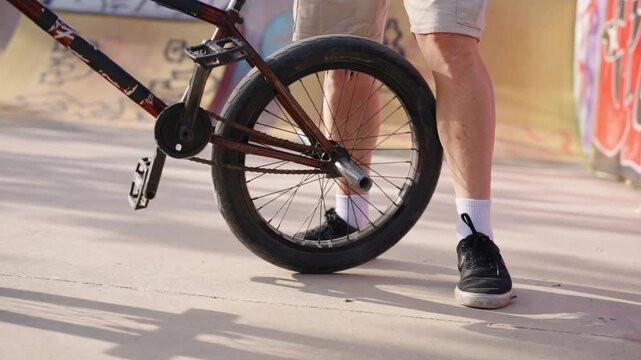 BMX rider lifting bicycle from ground with a quick foot kick before starting to ride at skatepark in slow motion