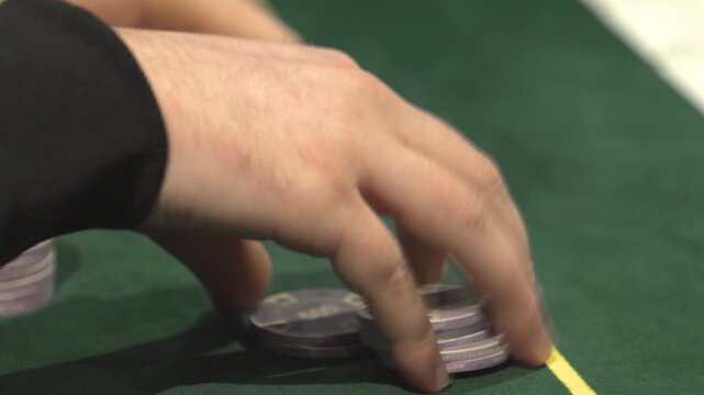 Close-up shot of a poker player playing with casino chips at a gaming table. Gambling, betting, poker and casino entertainment concept footage.