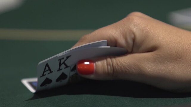Close-up shot of a woman checking poker cards at a casino table. Ace-King poker hand, gambling, betting and Texas Hold&rsquo;em concept footage.