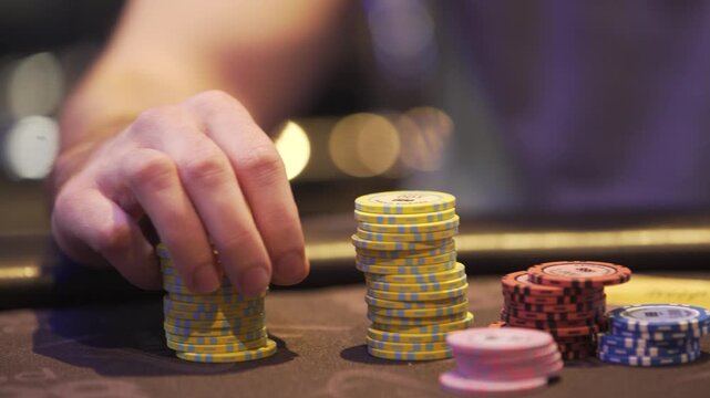 Close-up shot of a casino player arranging poker chips at a gaming table. Gambling, betting, poker strategy and casino entertainment concept footage.
