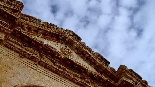 Low angle timelapse of the ornate Roman frieze and pediment at Jerash, Jordan. Detailed ancient architecture of the Decapolis city under a dynamic sky with moving clouds during the day