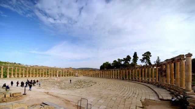 Daylight timelapse of the Oval Plaza in the ancient Roman city of Jerash, Jordan, showing tourists walking through the historic colonnaded square under a moving cloudy sky