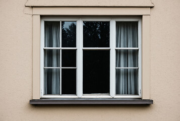 Fototapeta premium Classic wooden window on a beige stucco wall with white curtains