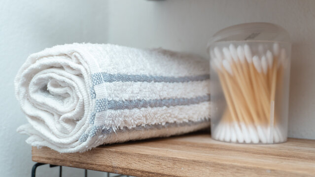 Toalla enrollada y cotonetes en repisa de ba&ntilde;o minimalista