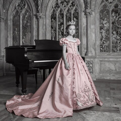 Fototapeta premium Monochrome Piano Lady. In A Gothic Room, The Young Princess Stands Before An Old Piano Wearing A Luxurious Pink Dress With Long Train