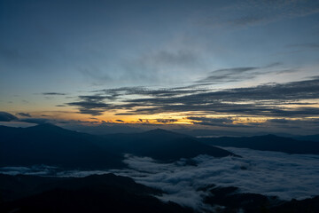 Fototapeta premium Early morning sunrise with mountain silhouette and clouds, calm natural landscape filled with morning mist.