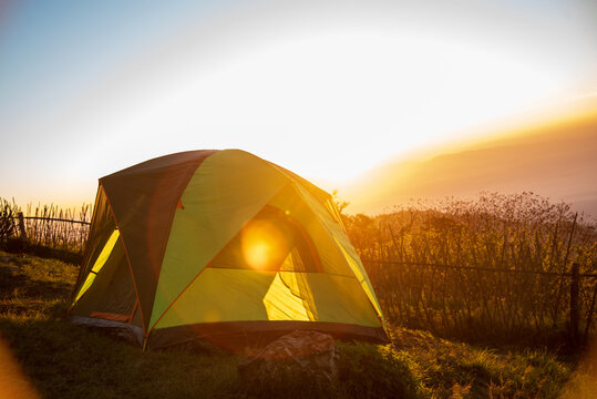 Tent camp in nature background with sunrise on top of mountain. Tent Camping trip outdoor hiking mountain hill. Adventure Travel wildness flare sunlight. Picnic tent green nature campground in forest
