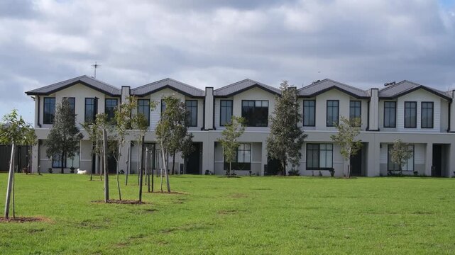 A row of modern, newly constructed two-story townhouse residences in the outer western suburb of Truganina, Melbourne, Australia. A person walking his dog along a shared green public space