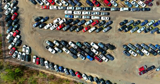 Many cars are parked in large lot with area is near trees appears to be busy some spaces are filled while others are empty.