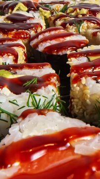 Close up of fusion sushi rolls topped with dark glaze and sesame seeds, served with fresh raspberries and chopsticks on a dark wooden board.
