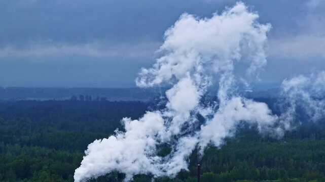 Cinematic aerial shot of a modern sawmill facility in Latvia with thick white smoke rising from a chimney against a lush green forest background.