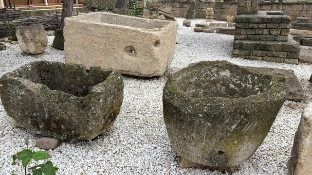 Stone bowls of different sizes are placed in a historical area with a gravel floor. Surrounding walls are made of stone, adding to the ancient atmosphere. A quiet space invites exploration.