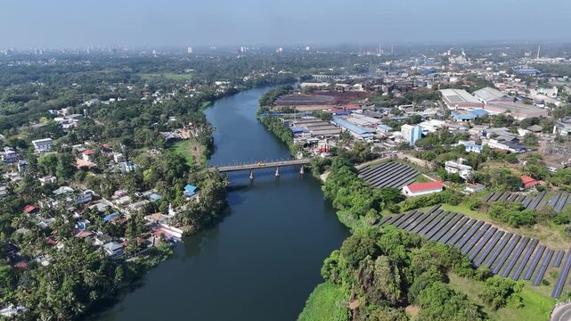 Cinematic aerial view of a periyar river flowing through lush tropical landscapes, with bridges connecting dense residential areas, layered greenery, and calm reflective waters beneath bright daylight