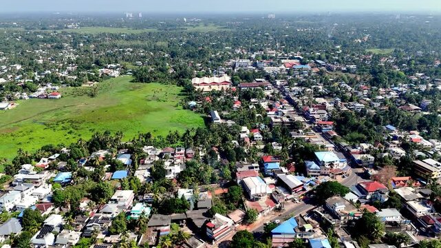 Cinematic aerial view of Aluva Kerala showcasing dense tropical neighborhoods, open green fields, and palm-covered landscapes blending seamlessly into a vast urban horizon.