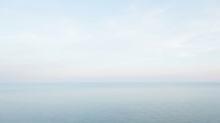 Fototapeta premium The image shows a vast, calm sea meeting a pale blue sky. The horizon line is indistinct, blending the water and sky into a seamless transition.