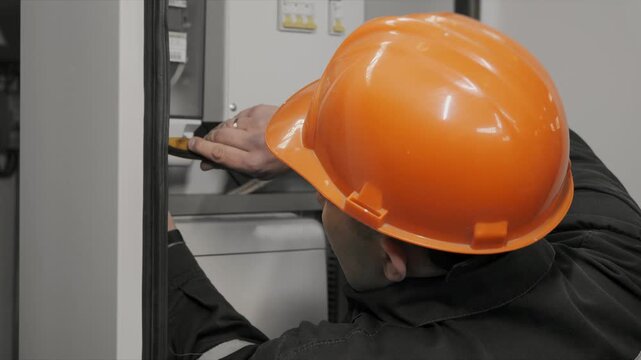 Industrial electrician performing maintenance and inspection of electrical control cabinet equipment in modern manufacturing plant environment