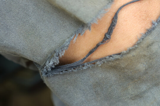 Close up detail of torn grey denim jeans revealing skin underneath showing distress and wear expressing rugged casual unkempt aesthetic in modern fashion style