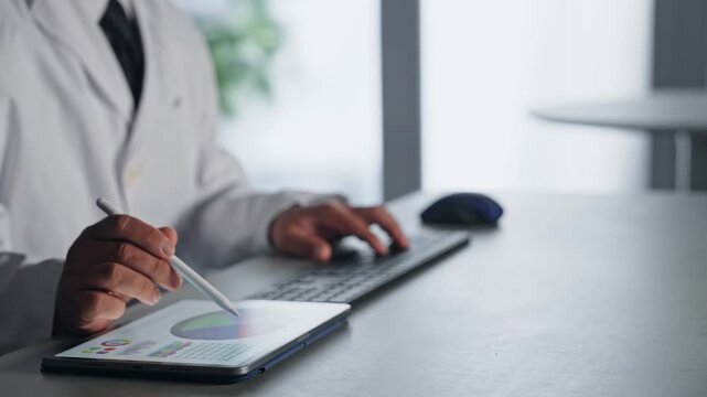 A man in a white coat working using a computer and a tablet PC.