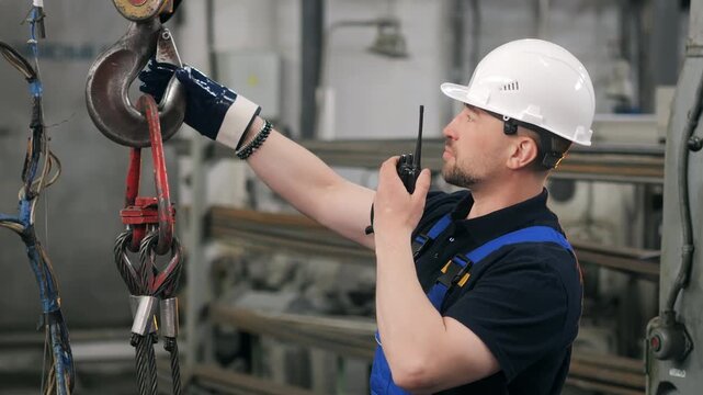 Factory worker using radio remote control to operate overhead crane and lifting hook during material handling process in modern manufacturing facility