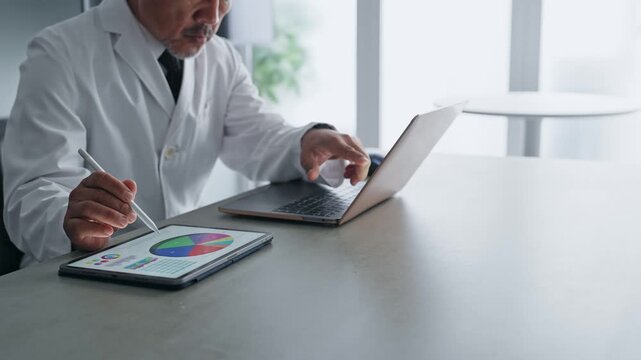 ノートパソコンとタブレットPCを使って作業する白衣の男性