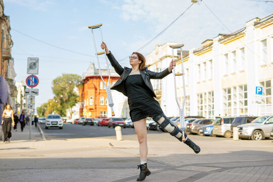 Young girl with a plastered foot in the orthosis and with crutches on a walk in the city