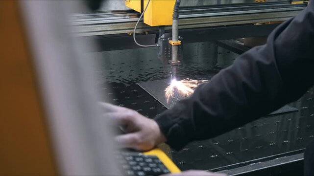 Industrial worker operating CNC plasma cutting machine while monitoring automated steel sheet cutting process in modern metalworking workshop