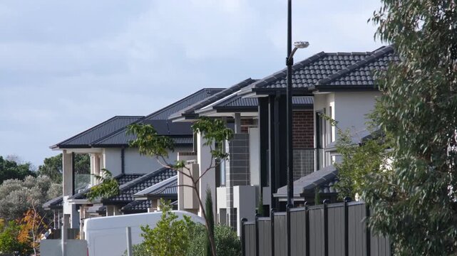 A row of generic, copy-paste modern two-story houses with uniform dark grey tiled roofs in the sprawling suburb of Truganina, Melbourne, Australia. Concept of urban sprawl and lack of individuality