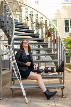 Young girl with a plastered foot in the orthosis and with crutches on a walk in the city