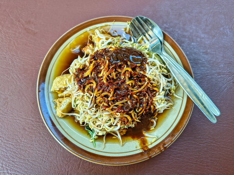 A plate of "lontong balap" with dark sauce served simply with a fork and spoon.