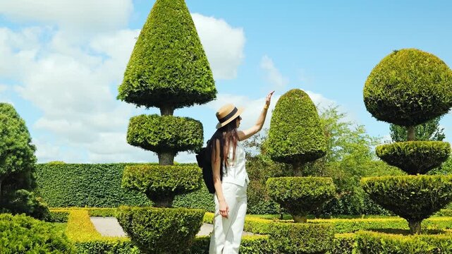 Young woman in white outfit touching topiary in French style garden summer