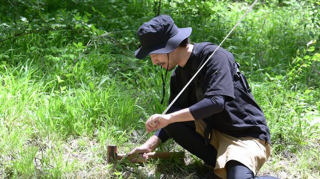 森林でテントを張るペグを打つ楽しむ男性と自然体験のアウトドアイメージの動画