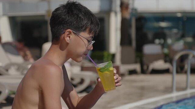 Young vacationer sipping refreshing citrus drink near swimming pool during sunny tropical holiday