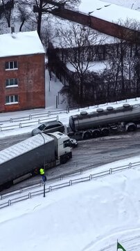 Aerial vertical parallax shot of winter truck accident with jackknifed trailer on slippery icy road and yellow rescue tractor arriving in Latvia