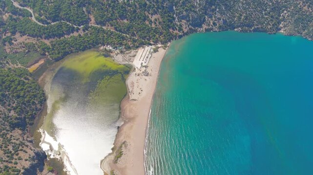 Dalyan, Turkey. Iztuzu Beach, a narrow sandbar separating turquoise Mediterranean waters from the Dalyan River delta, with organized rows of sun loungers and a beach facility under bright summer sun.