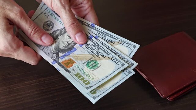 Woman counting 100 US dollar banknotes over a table with a leather wallet. American cash money, concept of money circulation, financial security. Real time motion video.